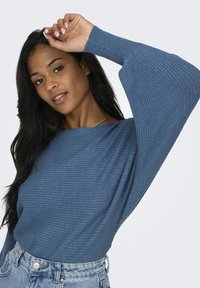 Pull bleu à côtes avec des manches larges, fabriqué dans un matériau doux, associé à un short en denim taille haute. Présente une coupe décontractée.