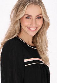 Blusa nera a maniche lunghe con tessuto testurizzato, caratterizzata da accenti ricamati colorati sul petto. Scollo elegante e vestibilità ampia.