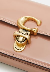 Lyserød patenteret læderpung med en guldfarvet C-formet spænde og hardware, samt kontrasterende stikninger langs kanterne.