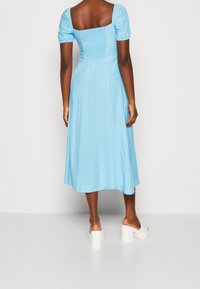 Jasnoniebieska sukienka midi z bufkami, kwadratowym dekoltem, marszczonym górnym częściami i zwiewną spódnicą. Białe sandały na platformie dopełniają strój.