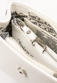 Interno di una borsa in finta pelle bianca con numerosi scomparti con zip, accessori in argento e una fodera in tessuto con motivo. Presenta un tirazip decorativo.