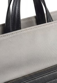 Primer plano de una bolsa de lona gris con asas de cuero negro y una cremallera negra a lo largo del borde inferior de la sección visible.