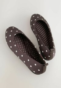 Braune flache Schuhe mit weißen Punkten, rundem Zehendesign, strukturierter Innenausstattung und einer kleinen Lasche am Absatz für einfaches An- und Ausziehen.