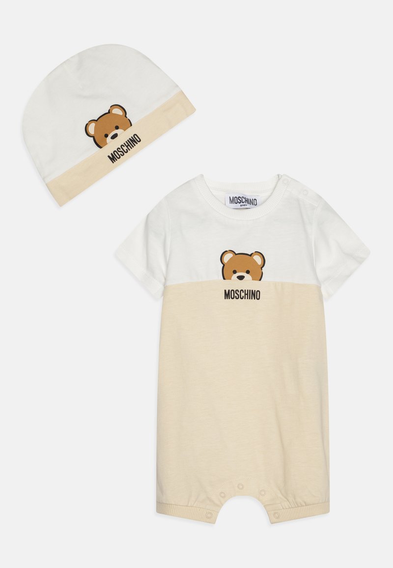 Tutina Moschino per bambino con berretto coordinato. Parte superiore bianca con grafica dell'orso, parte inferiore beige, chiusura a scatto nella parte inferiore, materiale in cotone morbido.