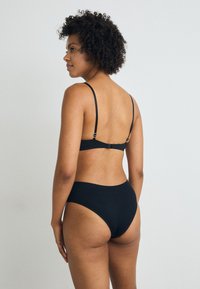 Black bikini set featuring a ribbed texture. The top has thin straps and a clasp at the back, paired with high-waisted bottoms.