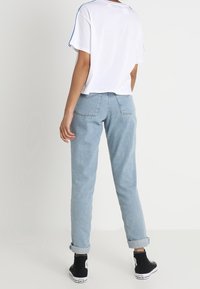 Camiseta blanca recortada con rayas azules, jeans de tiro alto azul claro y zapatillas negras. Puños enrollados en los jeans, ajuste casual.