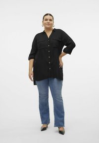 Sort skjorte med knapper og to brystlommer, trekvartærmer, sat sammen med blå flared jeans og sorte spidse hæle.