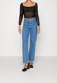 Schwarzer Spitze-Bodysuit mit langen Ärmeln und quadratischem Ausschnitt, kombiniert mit hochgeschnittenen blauen Straight-Leg-Jeans und schwarzen High Heels.