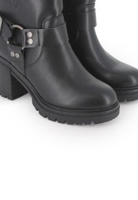 Botas de cuero negro hasta el tobillo con un tacón grueso, correas ajustables y acentos de metal, que cuentan con una suela estriada para mayor agarre.