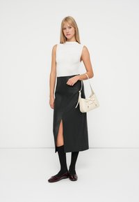 Λευκό τοπ χωρίς μανίκια, μαύρη δερμάτινη midi φούστα με πλαϊνό σκίσιμο, μαύρες κάλτσες μέχρι το γόνατο, μπορντώ φλατ παπούτσια, και μια μικρή μπεζ τσάντα.