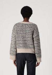 Pull en tricot avec un motif géométrique crème et marine, col rond et bords-côtes aux poignets et à l'ourlet. Texture douce et coupe décontractée.
