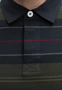 Chemise sombre à col avec des rayures horizontales grises, rouges et olive, boutonnée au niveau du col supérieur.