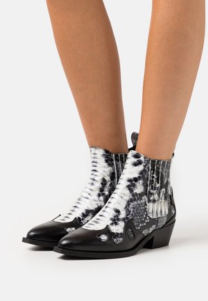 Bottes en cuir à motif serpent noir et blanc, montantes jusqu'à la cheville, avec des orteils pointus et de petits talons carrés, portées sur des jambes nues.