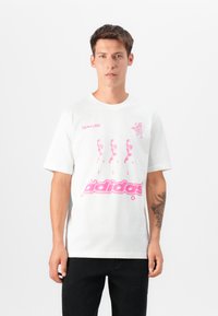 Hvit bomull T-skjorte med rosa grafisk design, tekst og figurer. Korte ermer og rund hals. Stylet med svarte bukser.