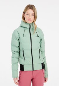 Lichtgroene donsjacks met capuchon, zwarte rits en accenten. Beschikt over elastische manchetten en een aansluitend ontwerp. Gedragen met roze broek.