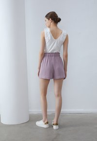 Haut sans manches blanc avec des épaules à volants, assorti à un short violet clair avec une taille élastique et des poches. Baskets blanches avec des accents dorés.