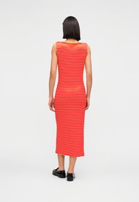 Μίντι φόρεμα με κόκκινες κα ι λευκές ρίγες, εφαρμοστή σιλουέτα, χωρίς μανίκια και μαύρα επίπεδα παπούτσια. Λείο, ελαστικό ύφασμα.