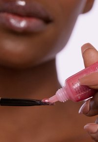 Glanzende roze lipgloss in een klein viala, met een zwarte applicator. Toont een glanzende textuur en subtiele glans.