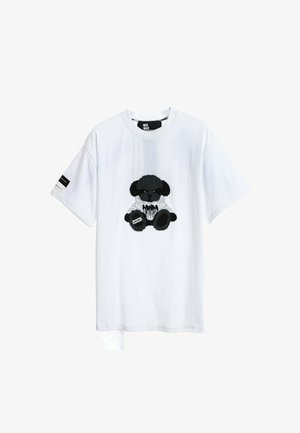 Camiseta de algodón blanca con un diseño de oso de peluche negro texturizado en el centro. Incluye una pequeña etiqueta negra en la manga izquierda.
