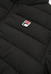 Gilet piumino nero con design trapuntato, caratterizzato da un logo ricamato prominente in rosso, bianco e blu sul petto. Dettaglio della cerniera visibile.