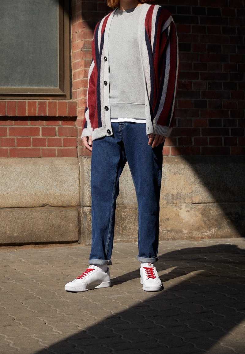 Cardigan lavorato a maglia a strisce rosse, bianche e blu navale sopra una felpa grigia; jeans blu; scarpe da ginnastica bianche con lacci rossi; outfit informale.