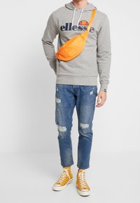 Grå huvtröja med logotyp, orange axelväska, slitna blå jeans och gula hög-top sneakers. Avslappnad outfit som kännetecknas av en blandning av färger.