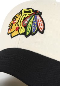 Cappello da baseball realizzato in tessuto avorio con visiera nera. La parte anteriore presenta un volto nativo americano ricamato in colori vivaci.