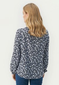 Blusa a maniche lunghe con un motivo geometrico blu e grigio, caratterizzata da una vestibilità rilassata, orlo arrotondato e polsini arricciati. Realizzata in tessuto leggero.