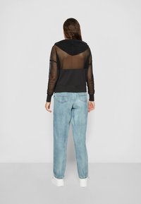 Sudadera de malla negra con un panel oscuro sólido; cuenta con capucha y mangas largas. Combinada con jeans sueltos de color azul claro y zapatillas blancas.
