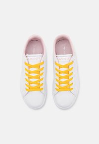 Bílé tenisky s žlutými tkaničkami, růžovou podšívkou a jemným detailem loga. Hladký materiál s klasickým atletickým designem a kulatou špičkou.
