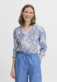 Modrá a krémová blůza s paisley vzorem, výstřihem do V a nařasenými rukávy, v kombinaci se světle modrými lněnými kalhotami na šňůrku. Texturovaná látka.