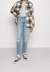 Camicia di flanella a quadri nei toni del marrone e bianco, top aderente grigio chiaro, jeans chiari strappati, sneaker verdi e bianche.