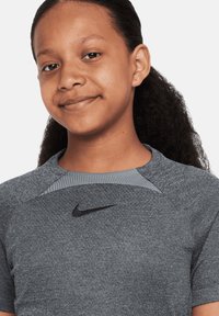 Graumeliertes Kurzarm-Sportshirt mit strukturiertem Kragen, das auf der Brust ein schwarzes Nike-Logo und eine glatte Stoffoberfläche aufweist.