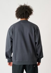 Dunkelgrauer Sweatshirt mit langen Ärmeln, gerippten Bündchen, lockerer Passform und Rundhalsausschnitt. Einfacher, strukturierter Stoff mit minimalen Details.