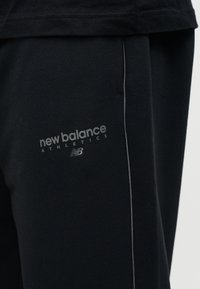 Κοντινό πλάνο μαύρου αθλητικού παντελονιού με ανακλαστικό λογότυπο New Balance Athletics και κάθετη επένδυση κατά μήκος της πλαϊνής ραφής.