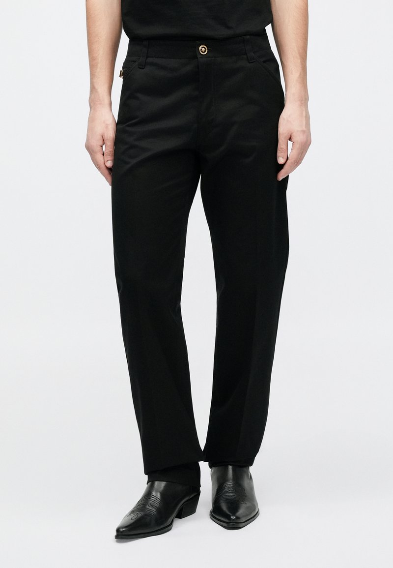 Svarta byxor med rak skärning, med en guldknapp och sidofickor. Tillverkade av mjukt tyg med en minimalistisk design.