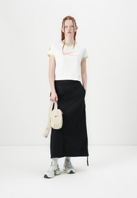 White cropped t-shirt with yellow accents and orange Nike logo, paired with a black long skirt and gray sneakers with green accents. Beige bag.