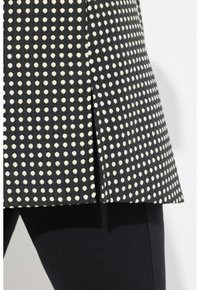 Tissu noir à pois blancs, doté d'un design plissé sur l'ourlet, associé à un pantalon noir pour un look coordonné.