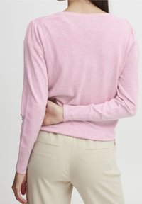 Suéter de punto rosa claro con puños acanalados y cuello redondeado. Presenta una textura sutil. Combinado con pantalones beige, mostrando vista posterior.
