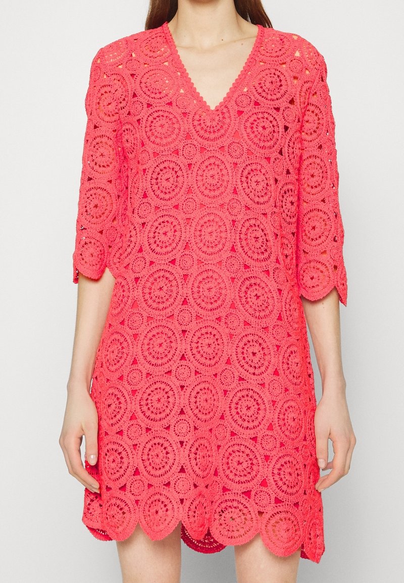 Vestido de ganchillo color coral con escote en V, mangas tres cuartos y patrones circulares. El dobladillo festoneado añade detalle a la tela texturizada.