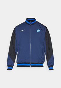 Nike jacket featuring a zip front, high collar, navy blue body with black sleeves and blue accents, and an embroidered logo on the chest.