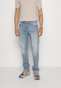 Jeans dritti di colore bleu chiaro in denim, abbinati a un top a maniche corte beige a costine e scarpe da ginnastica con un design spesso in grigio e rosa.