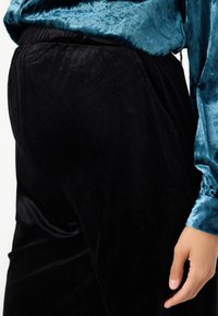Black velvet sweatpants with a smooth texture and elastic waistband, paired with a teal satin long-sleeve shirt featuring a subtle sheen.