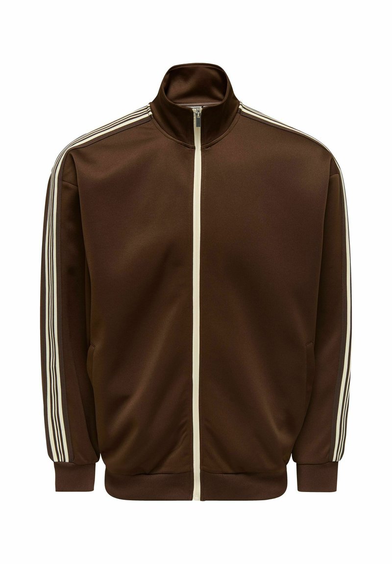 Καφέ φόρμα με λείο ύφασμα, με ψηλό γιακά, πλήρες φερμουάρ και λευκές πλαϊνές ρίγες στα μανίκια. Δύο πλαϊνές τσέπες.