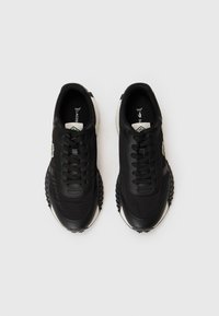 Black sneakers with a smooth leather upper, round toe, lace-up front, and textured rubber sole. Features green logo detail on side.
