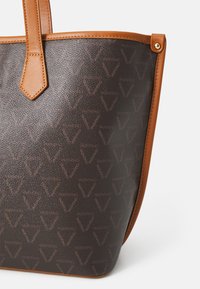 Rudas rankinė su tekstūruotu paviršiumi, odinėmis rankenomis ir pakartotiniu tamsesnės spalvos "Valentino" logotipo raštu. Papuošta šviesiai rudos spalvos detalėmis.