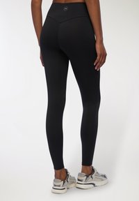 Czarne legginsy z wysokim stanem, bezszwowym designem i gładką, elastyczną teksturą, zestawione z szarymi butami sportowymi.