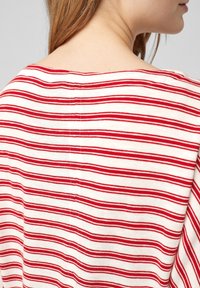 Rood-wit gestreepte stof met een zachte textuur, voorzien van een licht open achterkant bij de halslijn en zichtbare stikseldetails.