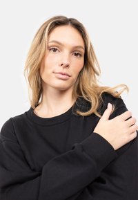Felpa nera con collo a giro e polsini a costine, caratterizzata da una vestibilità rilassata e una morbida texture del tessuto. Il modello indossa il capo.