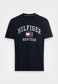 Námořnická modrá bavlněná tričko s bílým logem "HILFIGER" a nápisem "NEW YORK", s malým logem na levém rukávu. Klasický kulatý výstřih.
